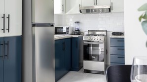 Een moderne keuken met roestvrijstalen apparatuur, blauw-witte keukenkastjes en een eethoek met een gedekte tafel voor twee.
