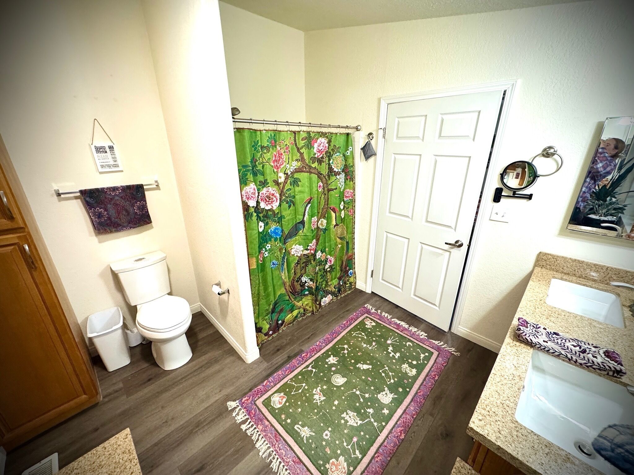 Bagno con il water, una tenda della doccia con motivo floreale, un tappeto verde e un lavandino con un asciugamano decorato.