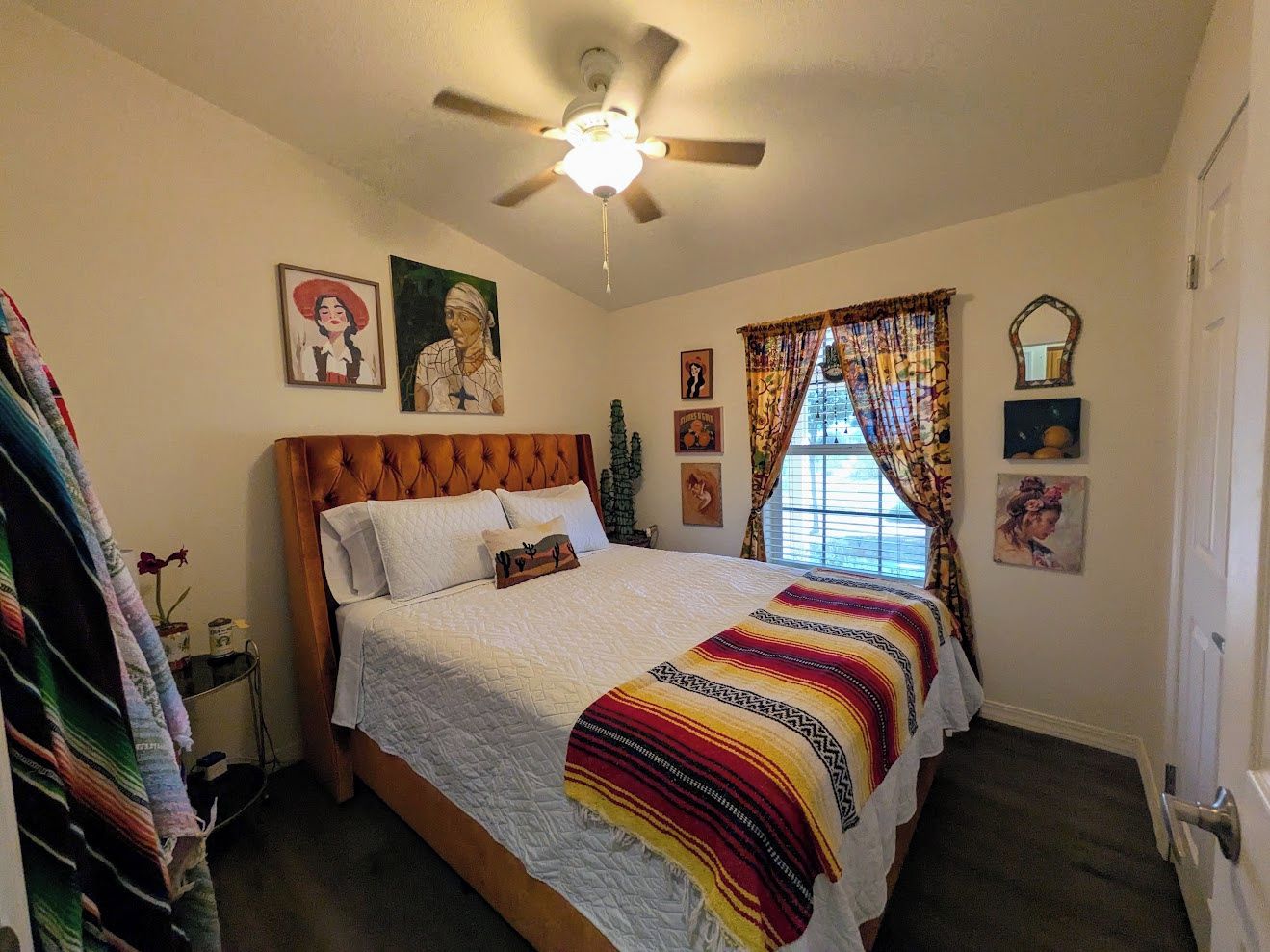 Un dormitorio con cama, ventilador de techo, ventana con cortinas y decoración en la pared.