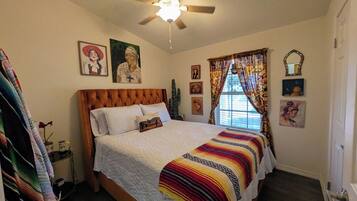 Un dormitorio con cama, ventilador de techo, ventana con cortinas y decoración en la pared.