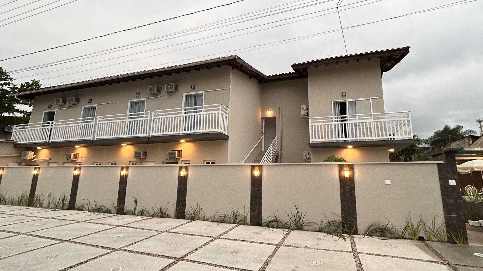 Un edificio de dos pisos con balcones, entrada protegida por un portón e iluminación exterior.
