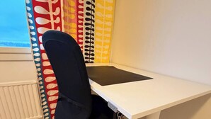 En modern kontorsstol med en svart, nätförsedd rygg och hjul, placerad framför ett vitt skrivbord med tangentbord och mus.