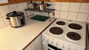 Ett kompakt kök med en spis, en ugn och en slow cooker på bänkskivan.