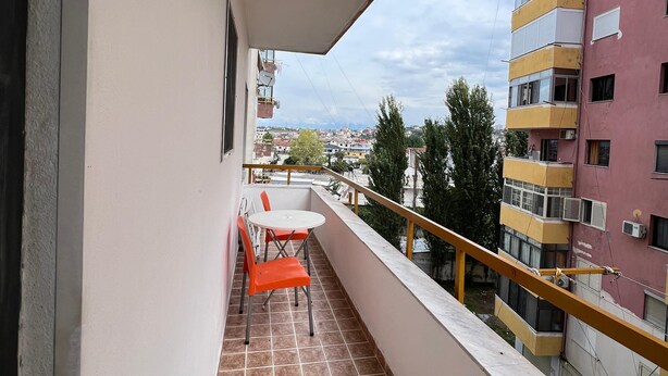 En balkon med flisegulv, et lille bord og to orange stole.