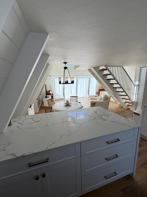 A modern kitchen with a marble countertop, white cabinetry, and a chandelier.