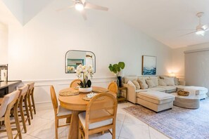 Ein modernes Wohnzimmer mit Essbereich, mit einem runden Holztisch, Korbstühlen, einem beigen Sofa und einem großen Spiegel an der Wand.