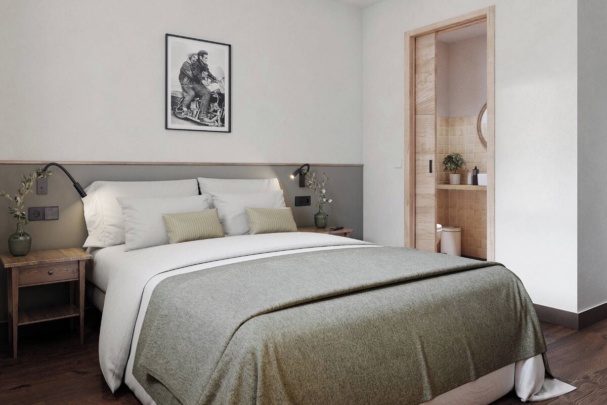 A modern bedroom with a bed, bedside tables, a nightstand, a framed picture on the wall, and a wooden wardrobe.