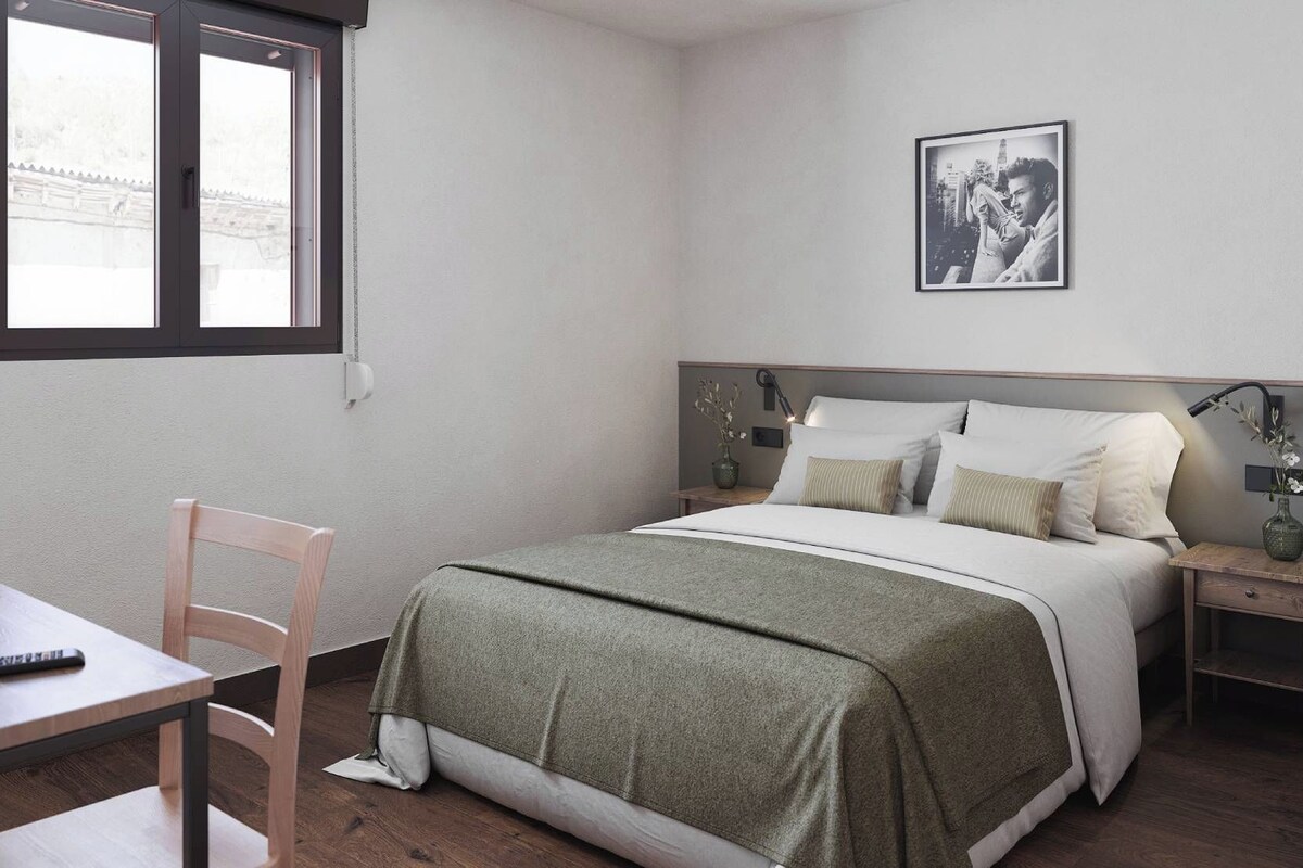 A bedroom with a bed, bedside tables, a nightstand, a chair, a desk, and a window.