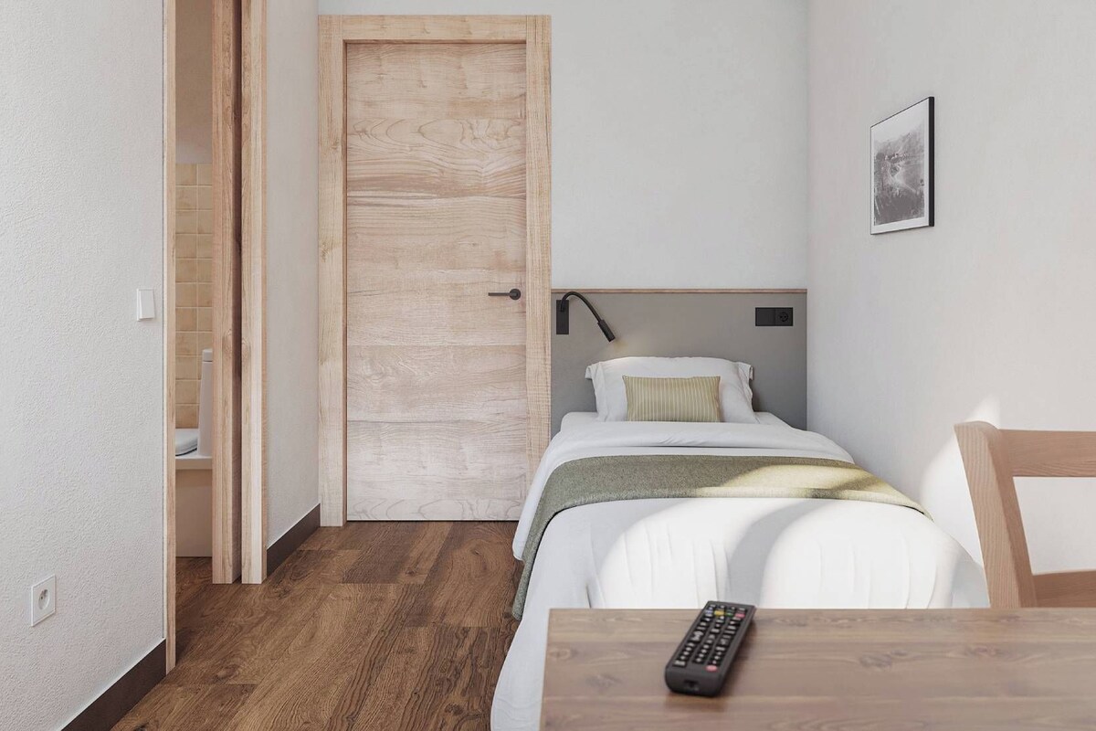 A small, neatly arranged bedroom with a single bed, a bedside table, and a chair.