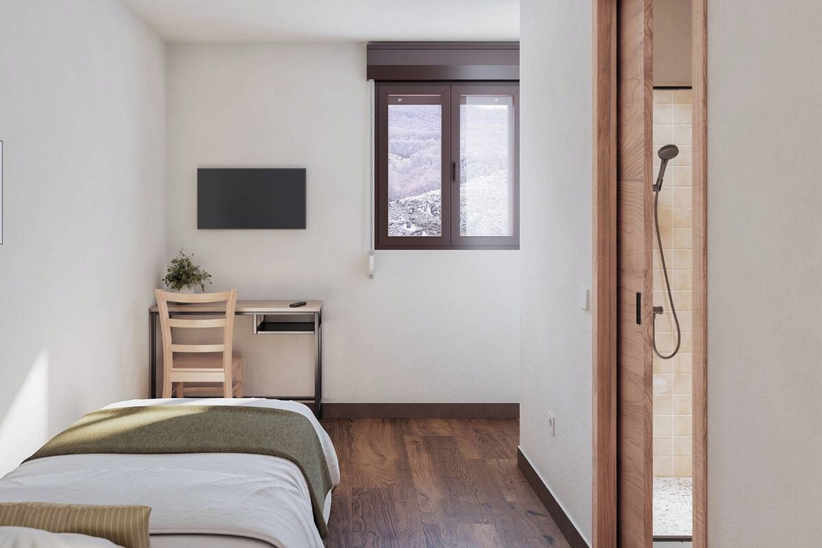 A bedroom with a bed, a desk, a chair, a TV, and a window with a view of a snowy landscape.