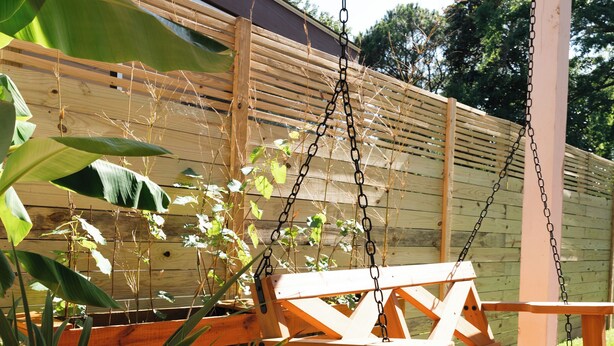 Een houten terras met een schommel en plantenpotten.