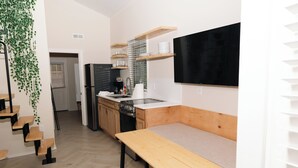 Een compacte keuken met een houten bankje, inbouwkasten en een zwarte televisie aan de wand.