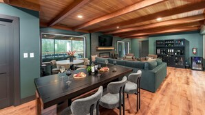 Un salón espacioso con techo de madera, una mesa de comedor con copas de vino y comida, una chimenea y una zona de estar acogedora.