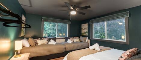 Un dormitorio con dos camas, ventilador de techo y ventanas amplias.