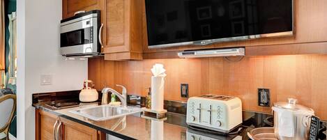 A modern kitchen with wooden cabinets, a built-in microwave, a large flat-screen TV, a toaster, and a slow cooker.