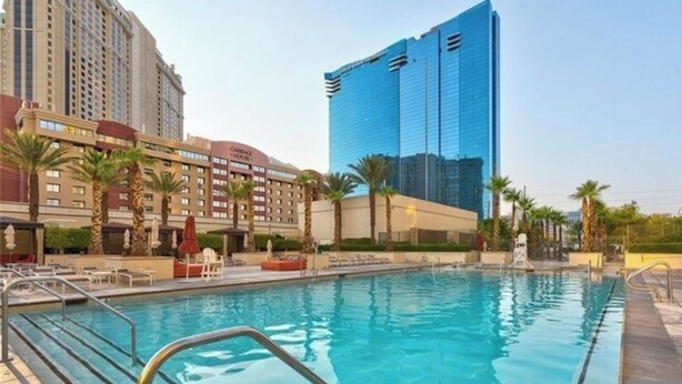 A hotel with a swimming pool, palm trees, and modern buildings in the background. - Vintage Lair at Signature (Las Vegas)
