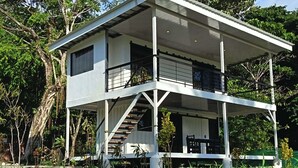 Una casa a due piani con un balcone, una scala e un piccolo angolo relax all'aperto.