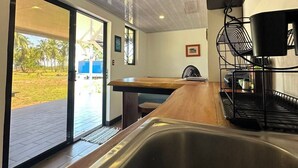 Una cucina moderna con lavello in acciaio inox, piano di lavoro in legno e vista su un giardino tramite ampie porte scorrevoli.