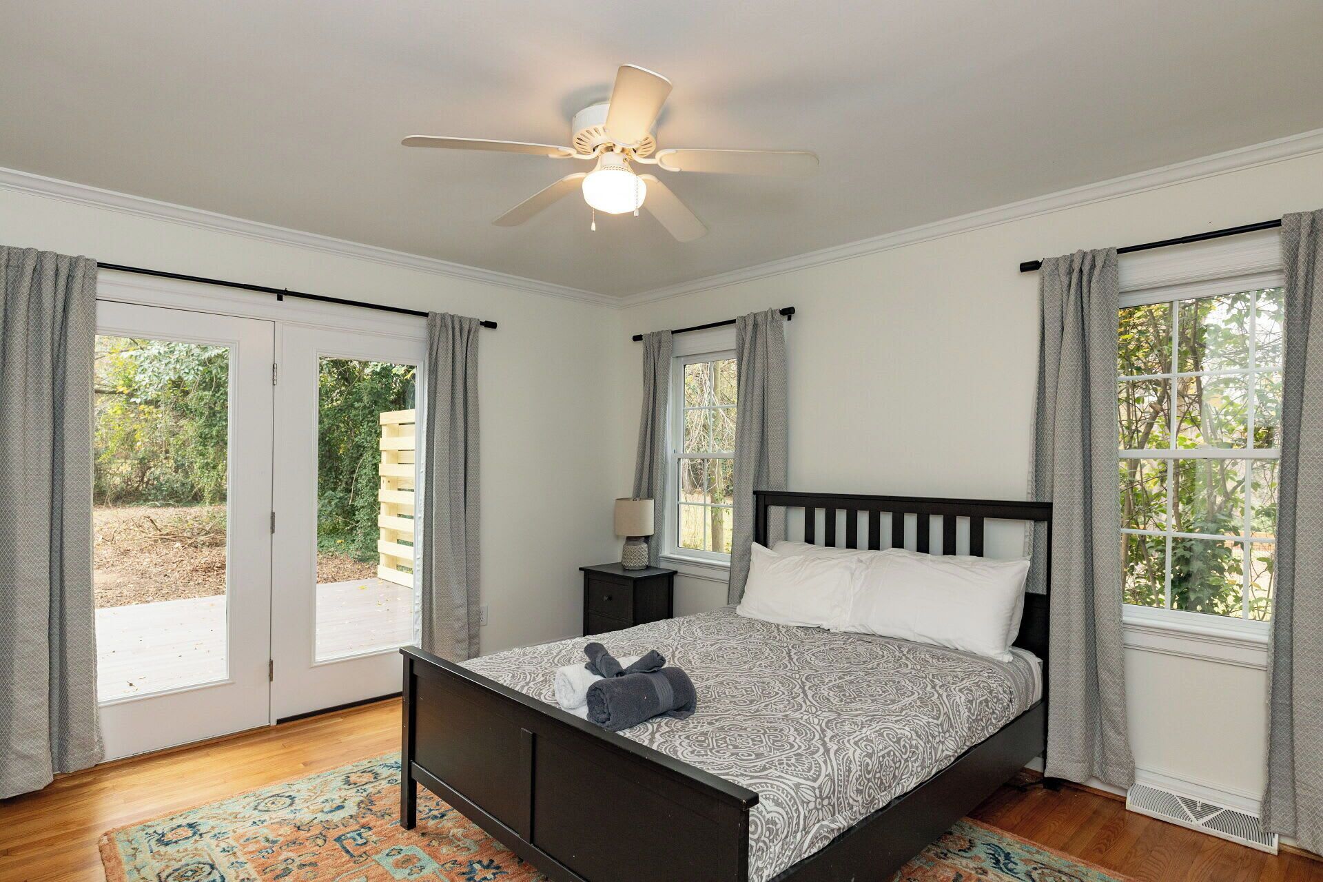 A bedroom with a bed, a ceiling fan, a nightstand, and a window with curtains.
