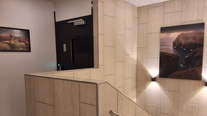 Et moderne interiør med en trætrappe, en sort elevator og et indrammet landskabsmaleri på væggen.