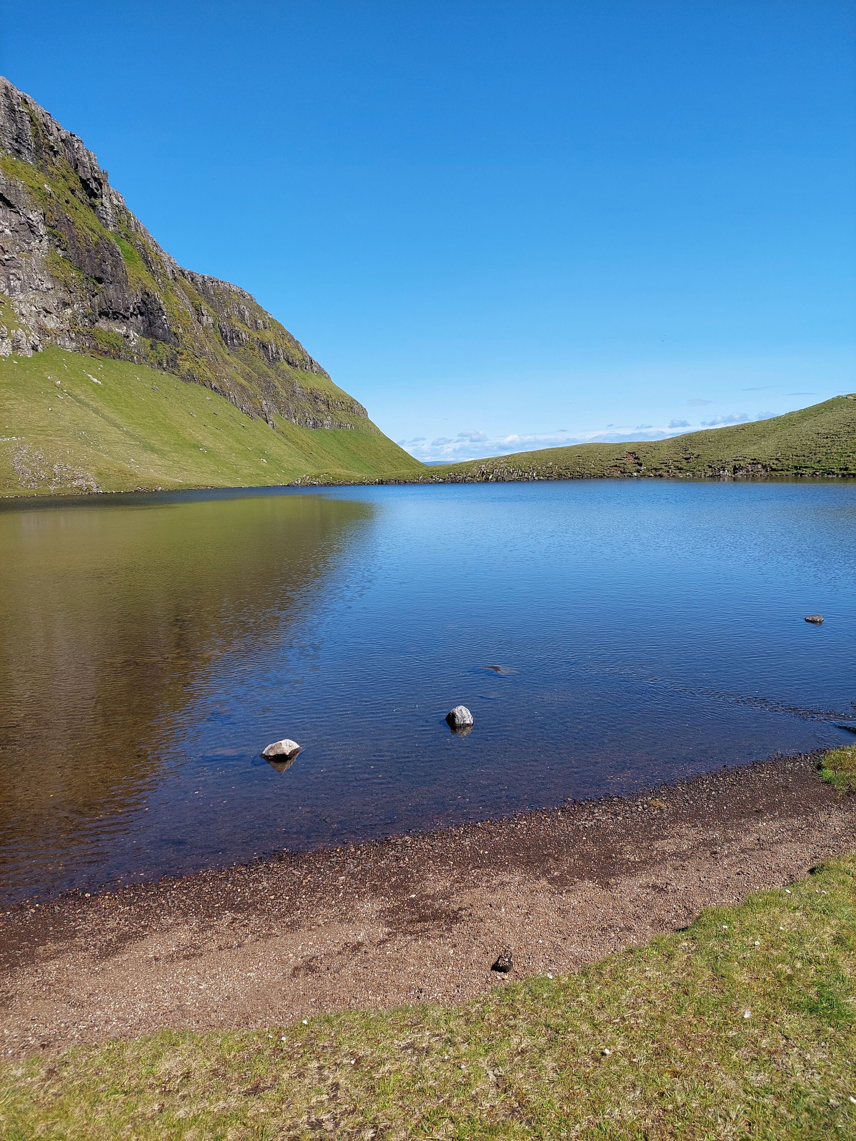 A calm lake surrounded by grassy hills and rocky cliffs.