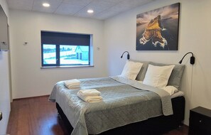 Een slaapkamer met een bed, een raam, een schilderij en een nachtkastje.
