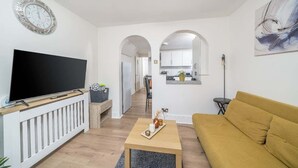 Ein Wohnzimmer mit Fernseher, Sofa, Couchtisch und einem durch einen Bogen sichtbaren Küchenbereich.