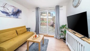 Ein Wohnzimmer mit einer Couch, einem Tisch, einem Fernseher und einer Schiebetür zu einem Außenbereich.