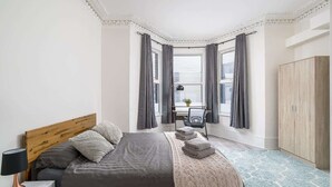 Ein Schlafzimmer mit Bett, Nachttisch, Lampe, Fenster mit Vorhängen und Blick auf die Stadt.
