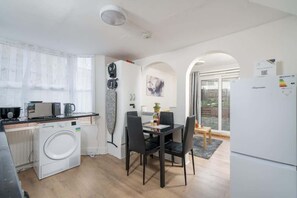 Een compacte keuken met een wasmachine, een magnetron en een eethoek met stoelen en een tafel.