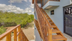 Un escalier en bois mène à un balcon d’où l’on peut admirer une vue sur des arbres verdoyants et un ciel dégagé.