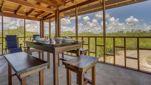 Un espace extérieur abrité, doté d’une table et de chaises, de grandes fenêtres et offrant une vue sur le paysage.
