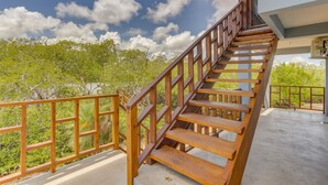 Un escalier en bois mène à un balcon d’où l’on peut admirer une vue sur des arbres verdoyants et un ciel dégagé.