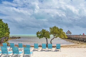 A beach with turquoise chairs, a wooden walkway, and a thatched-roof structure. - Ocean Pointe - Pool, Hot Tub, View, Beach, Parking (Tavernier)