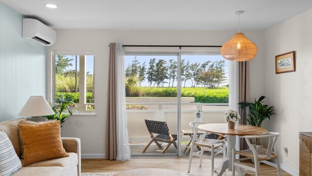 Ein modernes Wohnzimmer mit einer Couch, einem Tisch, Stühlen, einem großen Fenster mit Blick auf Grünflächen und einer Klimaanlage.