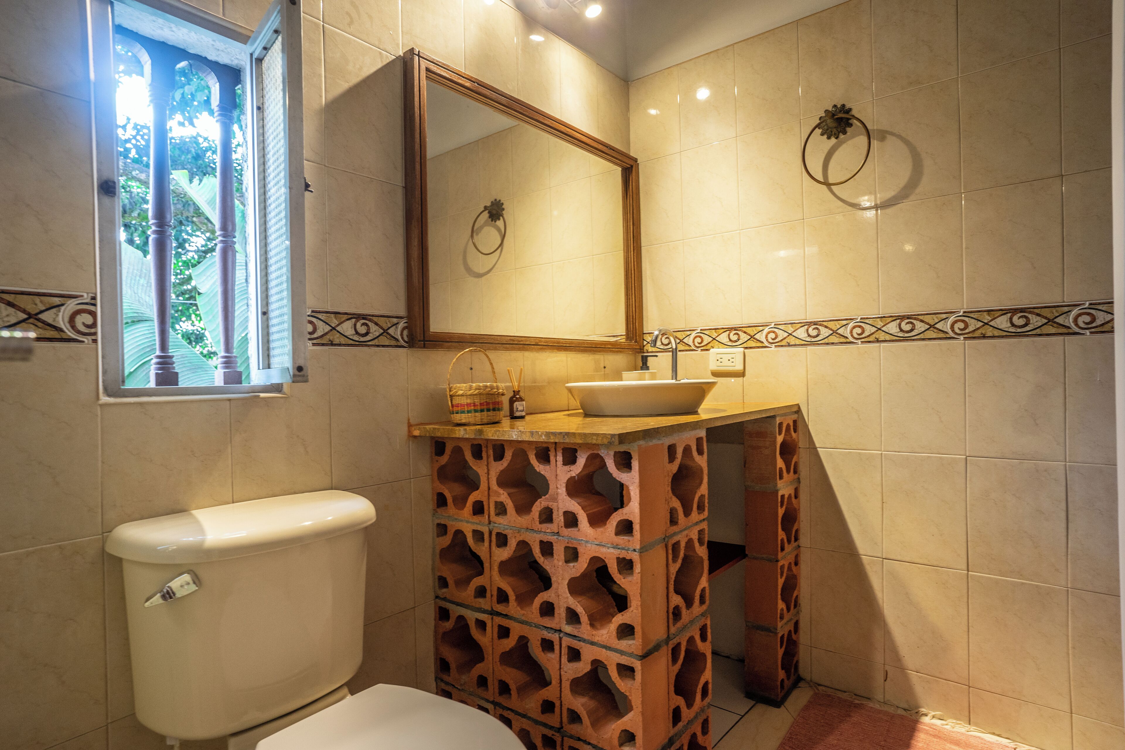 A bathroom with a toilet, a sink with a mirror above it, and a decorative tile border.