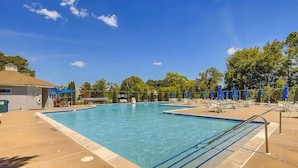 Ein rechteckiger Swimmingpool mit klarem, blauem Wasser, umgeben von Liegestühlen und Sonnenschirmen, mit einem Gebäude mit geneigtem Dach im Hintergrund.