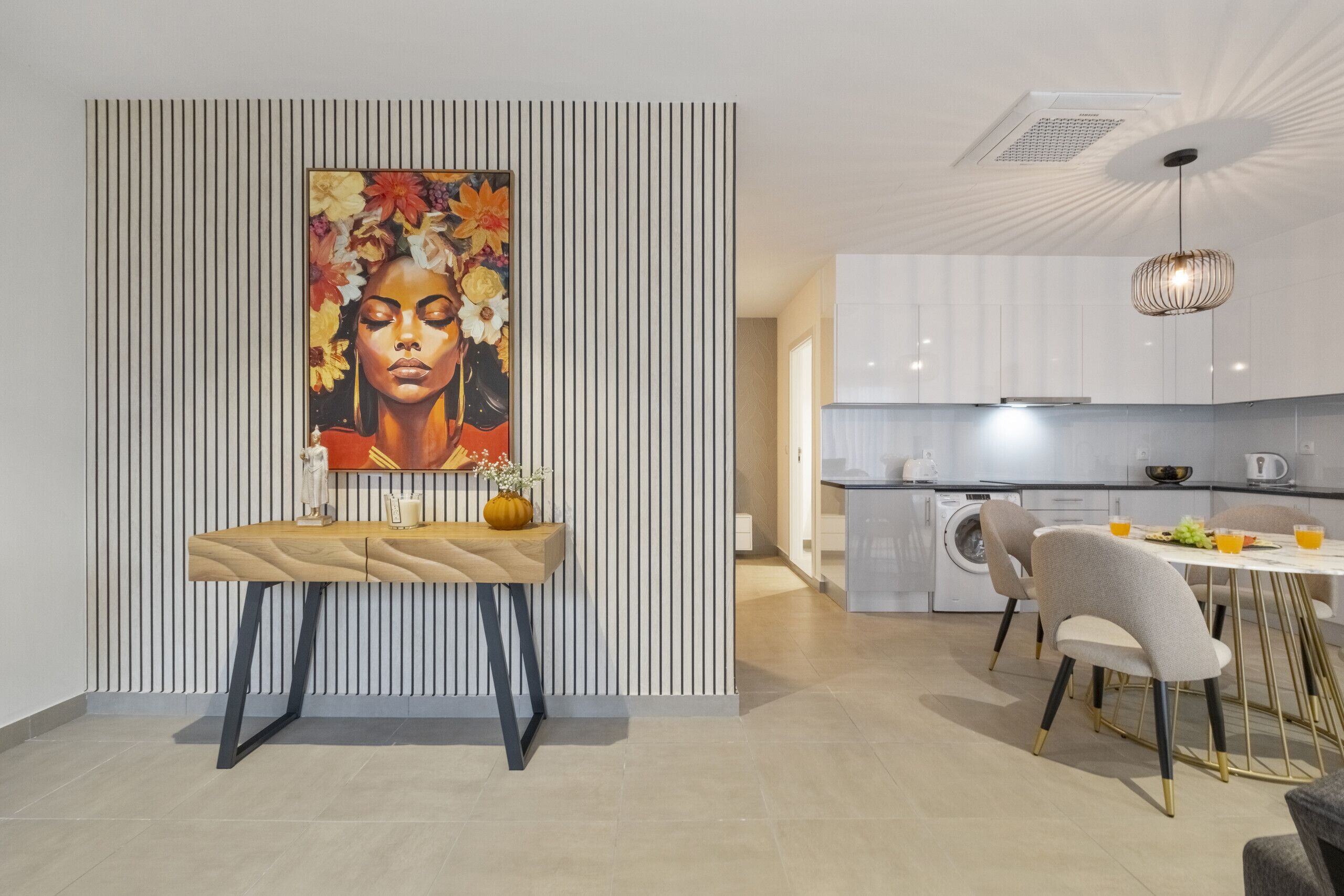 Une cuisine moderne avec des meubles blancs, un coin repas comprenant une table et des chaises, et un grand tableau accroché au mur.