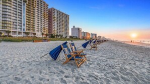 Une plage bordée de rangées de chaises longues, avec, en arrière-plan, une série d’immeubles de grande hauteur.