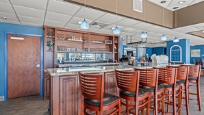 Un espace bar avec des tabourets de bar en bois, un comptoir avec de la verrerie et des luminaires suspendus.