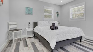 Een slaapkamer met een bed, een stoel, een nachtkastje en een wandlamp.