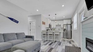 Een moderne woonkamer met een grijze bank, een keuken met witte kasten en een ingebouwde open haard.