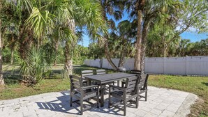 Een terras buiten met een tafel en stoelen, omgeven door palmbomen en een witte hek.
