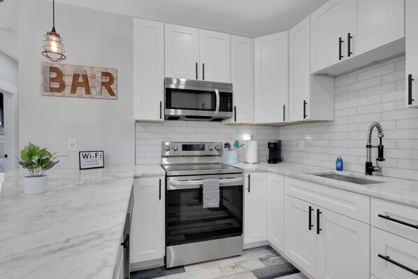 Une cuisine moderne avec des meubles blancs, un four en acier inoxydable, un micro-ondes et un évier.