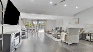 A spacious living room with a flat-screen TV, a sofa set, a coffee table, and a dining area with a table and chairs. - Spacious 4BR Home w/ Heated Pool & Pickleball Court on 5-Acre Estate (Naples)