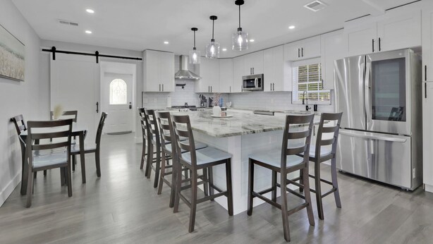 A modern kitchen with white cabinetry, a central island with bar stools, stainless steel appliances, and pendant lighting. - Spacious 4BR Home w/ Heated Pool & Pickleball Court on 5-Acre Estate (Naples)