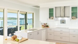 Une cuisine moderne dotée de grandes fenêtres, offrant une vue sur la mer, et un coin repas avec une table et des chaises.