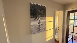En gang med trægulv, en dør der fører til et lyst rum, og et billede på væggen af en person på et paddleboard.