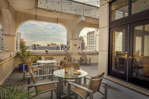 Terraza en la azotea con mesas y sillas, con vistas a un paisaje urbano con edificios y el letrero de Hilton.