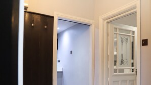 A hallway with a dark wooden door, a white door with decorative glass panels, and a small trash bin in the background. - Argyleluxe (Worsley)